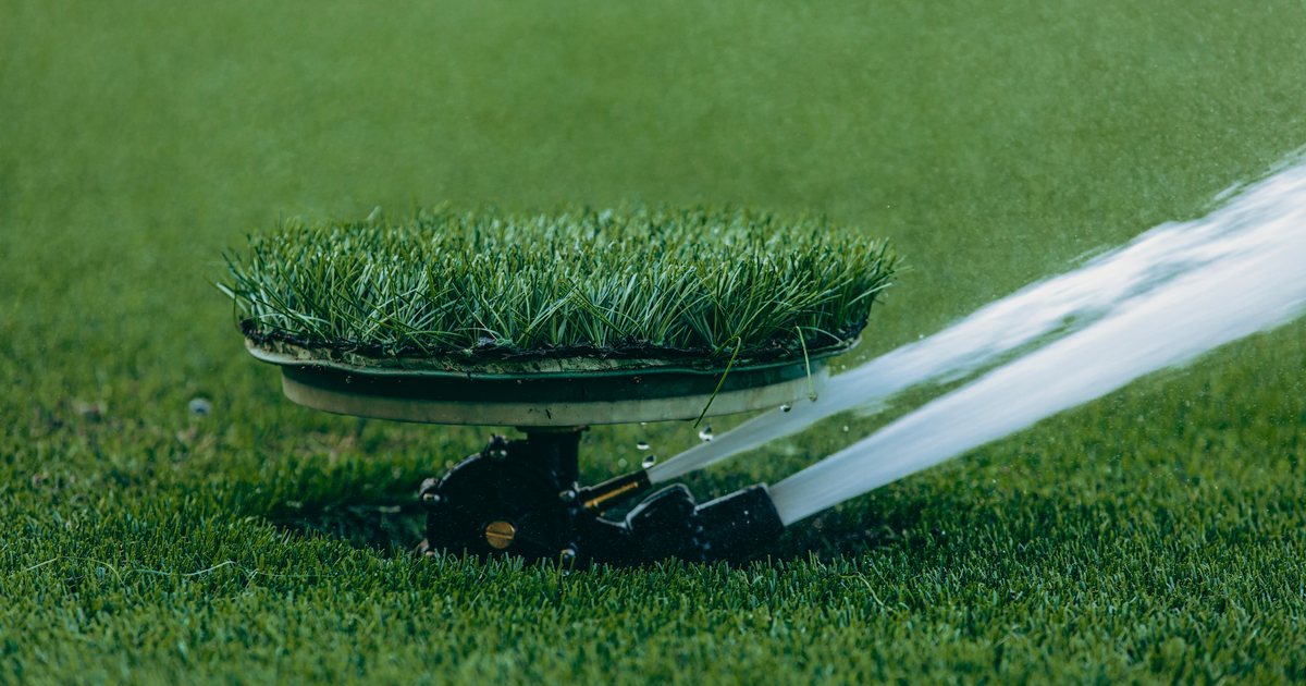 A sprinkler head spraying water across a green lawn