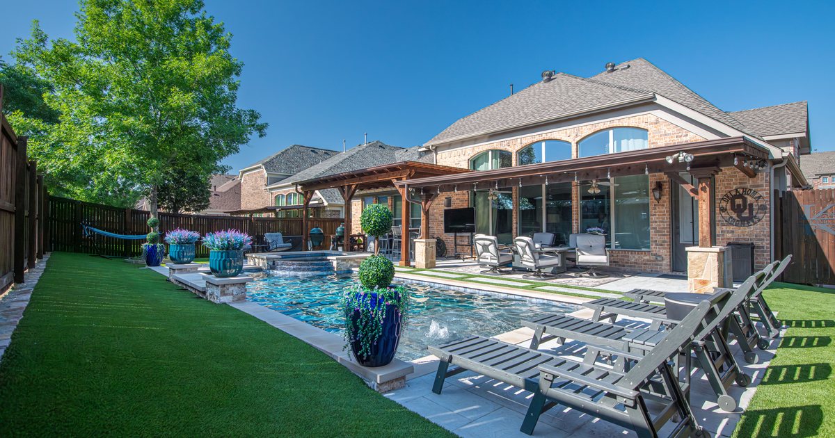 Artificial turf lawn bordering a backyard swimming pool and covered patio