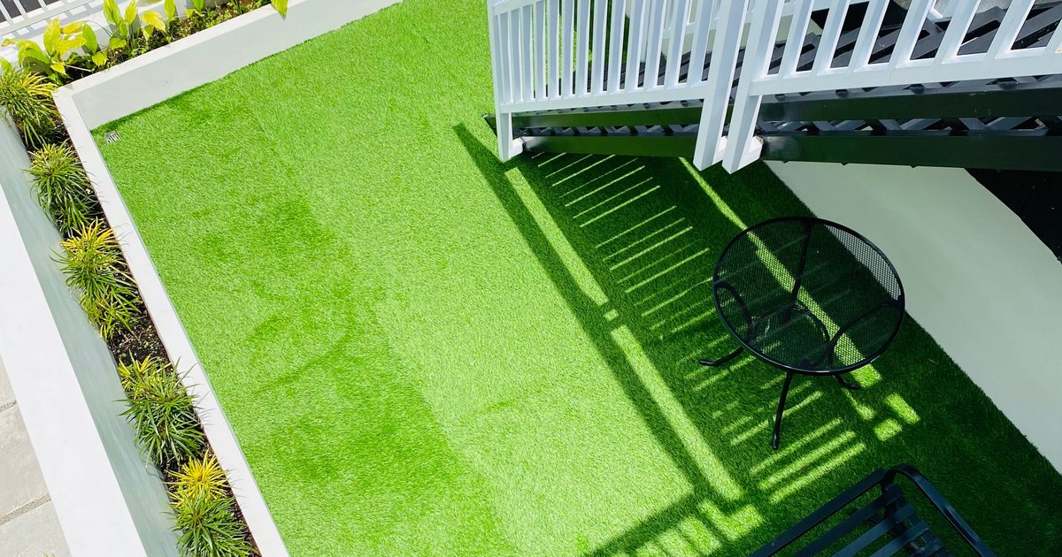 Aerial view of a rooftop terrace with artificial turf, white railings, and outdoor furniture